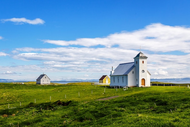 Flateyjarkirkja Kirche und ein paar Wohnhäuser mit Wiese im Vordergrund und Meeresfjord mit blauem Himmel im Hintergrund Flatey Island