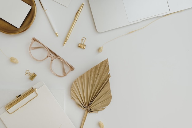 Flatlay aus goldenen Damenaccessoires und Büroartikeln, komfortabler Home-Office-Arbeitsplatz, Arbeit zu Hause, Laptop-Computer, Zwischenablage, Fächer, Blattstiel, Brillenklammern, Stift auf dem Tisch. Flache Lage von oben