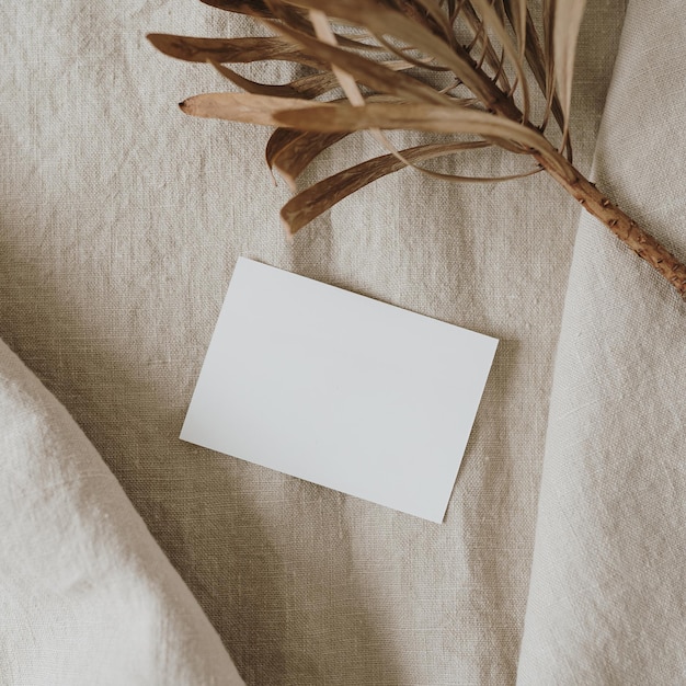 Flatlay aus leerer Papierkarte getrockneter Protea-Blume auf neutralem beige zerknittertem Leinentuch Geschäftsvorlage Draufsicht flach lag minimalistisches ästhetisches Luxus-Böhmen-Business-Branding-Konzept