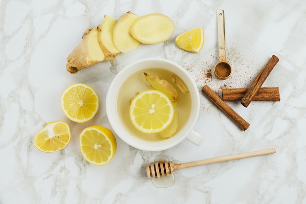 Flatlay de bebida saludable con limón, raíz de jengibre fresco, canela y jarabe de agave sobre fondo de mármol, resfriado natural o dolor de garganta