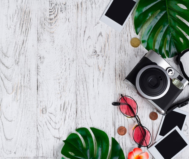 Flatlay con cámara, foto en blanco, monedas, gafas de sol, hojas en el escritorio blanco.