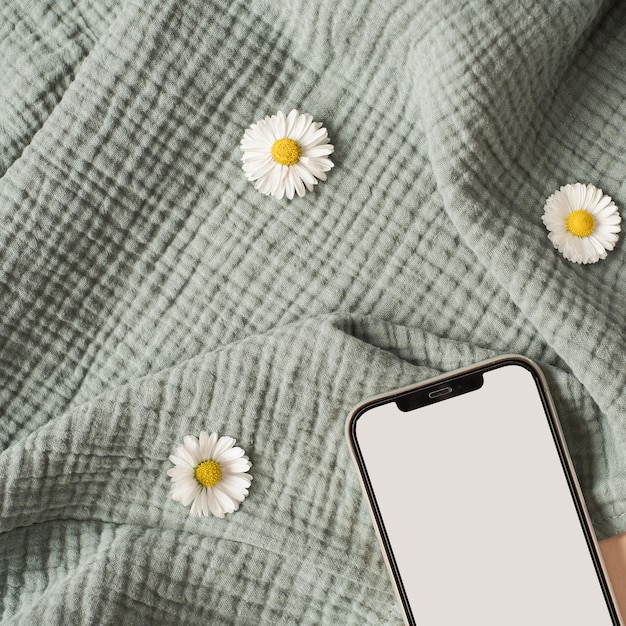 Flatlay de capullos de flores de manzanilla de teléfono móvil de pantalla en blanco tela de muselina aguamarina sobre fondo beige neutro Plantilla de blog de redes sociales estéticas con espacio de maqueta Vista superior plana