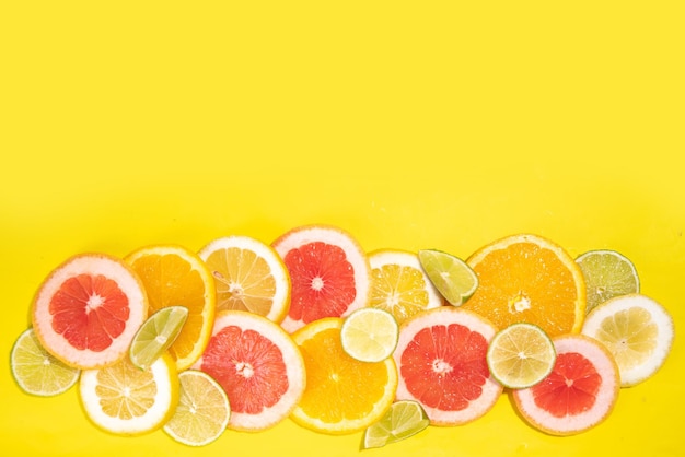 Flatlay colorido de fatias de frutas cítricas e folhas de palmeira tropical Toranja laranja limão limão fatias coloridas brilhantes em fundo amarelo Vista superior de fundo de férias de verão