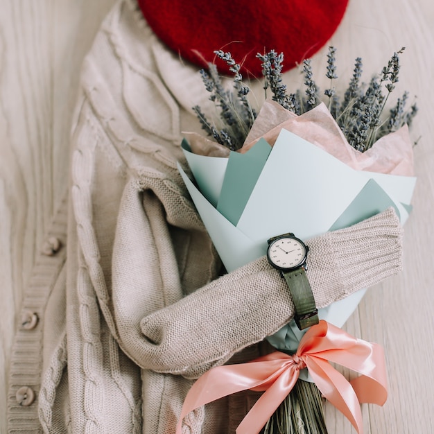 Flatlay creativo con ramo de flores, suéter beige y accesorios de mujer.