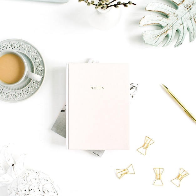 Flatlay da mesa da secretária do escritório em casa. Espaço de trabalho com caderno rosa pastel pálido e decorações em fundo branco. Camada plana, vista superior