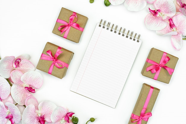 Flatlay de caixas de presente com fita rosa e flores da orquídea na opinião superior do fundo branco. Caderno de anotações ou redação de diário.