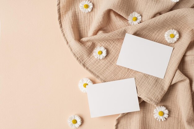 Flatlay de modelo de marca de negócios com estilo parisiense estético Cartão de folha de papel em branco com espaço de cópia de maquete botões de flores de camomila e pano de musselina em fundo bege neutro Vista superior plana leiga