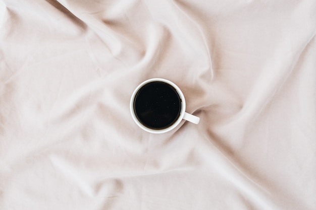 Flatlay der schwarzen Kaffeetasse auf pastellrosa Decke