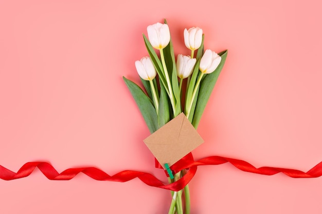 Flatlay Ein schöner Blumenstrauß, gebunden mit einem roten Band und einem Umschlag, isoliert auf pastellrosa Hintergrund