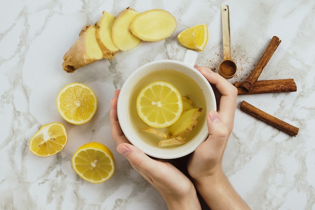 Flatlay eines gesunden Getränks mit Zitrone, frischer Ingwerwurzel, Zimtstangen und Agavensirup auf Marmorhintergrund, natürlicher Erkältung oder Halsschmerzen