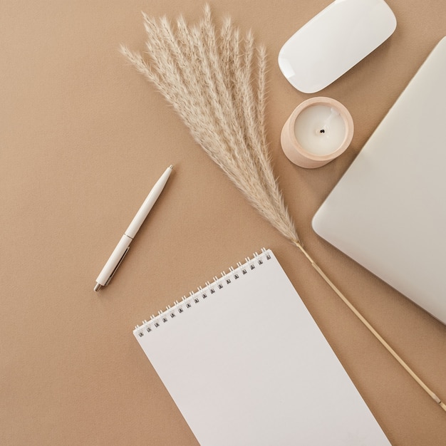 Flatlay eines Spiral-Flip-Notebooks mit leerem Papierblatt. Laptop, Pampagras, Briefpapier auf beige pfirsichfarbenem Pastellhintergrundtisch.