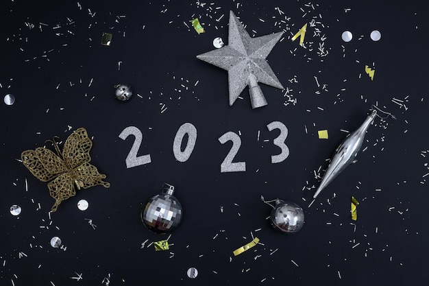 Flatlay festivo del año 2023 arreglado con brillantes adornos dorados y plateados sobre fondo negro