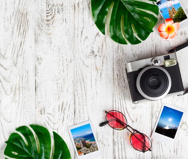 Flatlay mit Kamera, Foto, Sonnenbrille, Blätter auf dem weißen Schreibtisch.