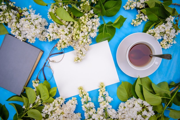 Flatlay con ramas de lila blanca, libro, vasos y té