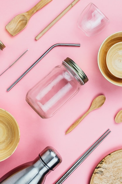 Flatlay de varios utensilios de cocina y vajilla sostenibles sin residuos: botellas de vidrio y metal, cuencos de bambú de madera, pajitas ecológicas, etc.en rosa