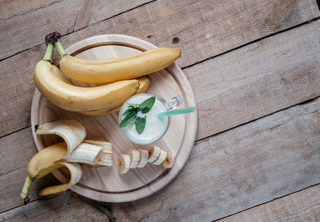 Flatlay de verano con batido de plátano o batido, hojas de menta y paja en un vaso sobre la mesa de madera oscura, bebidas de verano