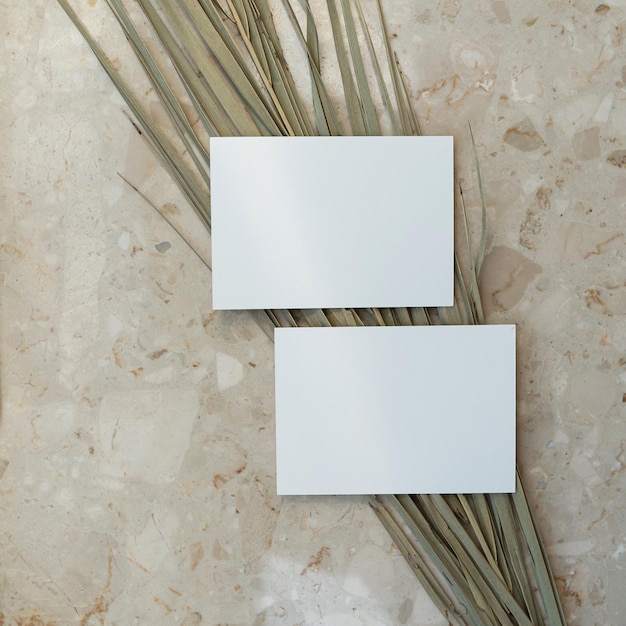 Flatlay von leeren Papierkarten trockener Palmblattstamm auf Marmorhintergrund Geschäftsvorlage Top-View Flatlay minimalistisches ästhetisches Luxus-Bohemien-Geschäftsbranding-Konzept