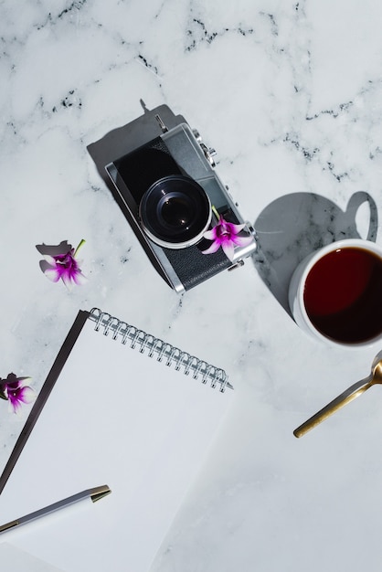 Flatlay von Vintage-Filmkamera und Notizbuch mit Stift auf Marmor