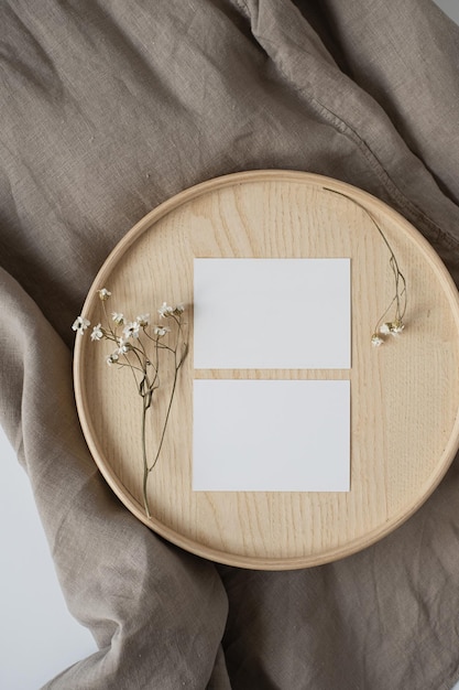 Flatlay von Visitenkarten aus leerem Papier mit Mockup-Kopienraum und Blumen auf Holztablett auf neutralem beigefarbenem Deckenhintergrund Ästhetische minimale Geschäftsvorlage für soziale Medien Flache Ansicht von oben