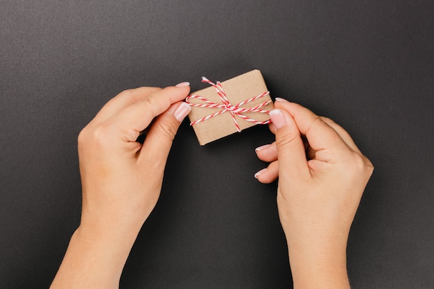 Flatlay weiblicher Hände, die eine Geschenkbox aus Kraftpapier auf schwarzem, isoliertem Hintergrund halten