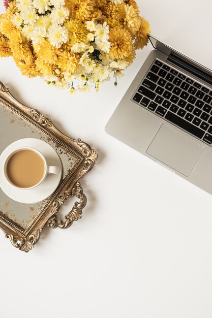 Flatlay weiblicher minimaler Arbeitsbereich mit Laptop, Kaffeetasse und schönem Blumenstrauß auf weißem Tisch. Draufsicht