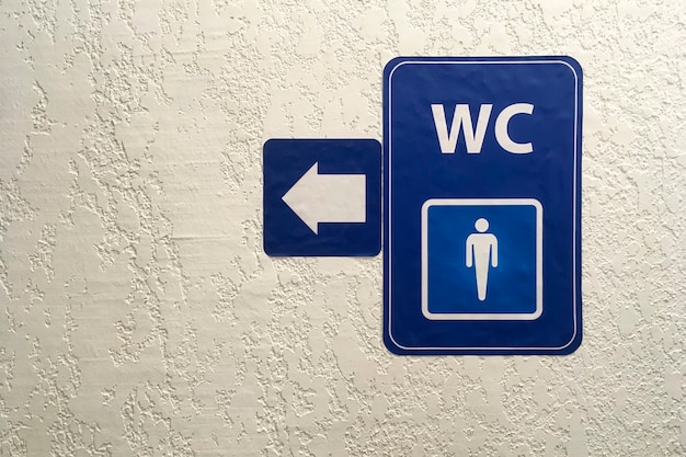 Foto flecha, puntero en la placa azul de baño público masculino signð ± en la pared enlucida. signo de aseo. concepto de baño .wc. disparo horizontal. copie el espacio. de cerca. adentro.