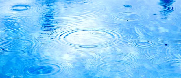 Flecken kreisen auf dem Wasser durch Regen. Regentropfen auf der blauen Wasseroberfläche des Pools. blaues Wasser Textur als Hintergrund. Langes Webbanner.