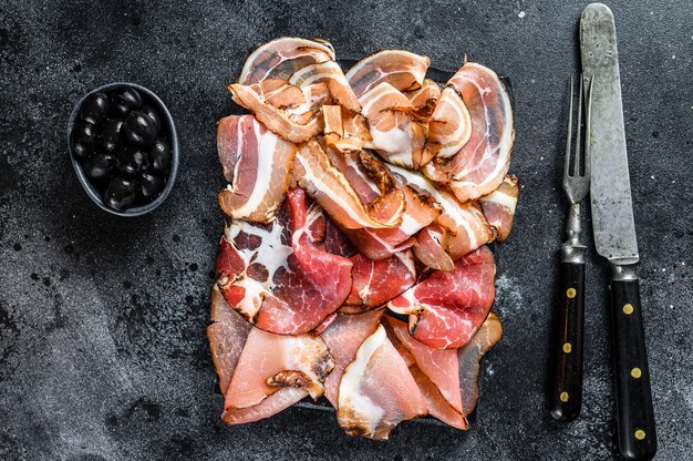 Fleisch Antipasti Platte, Pancetta, Salami, geschnittener Schinken, Wurst, Schinken, Speck. Schwarzer Hintergrund. Draufsicht.