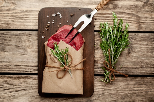 Fleisch aus einer Metzgerei in Papier eingewickelt. Ein Stück Rindfleisch auf Holz mit verschiedenen Gewürzen im rustikalen Stil