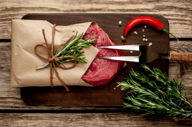 Fleisch aus einer Metzgerei in Papier eingewickelt. Ein Stück Rindfleisch auf Holz mit verschiedenen Gewürzen im rustikalen Stil