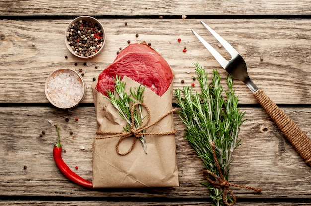 Fleisch aus einer Metzgerei in Papier eingewickelt. Ein Stück Rindfleisch auf Holz mit verschiedenen Gewürzen im rustikalen Stil