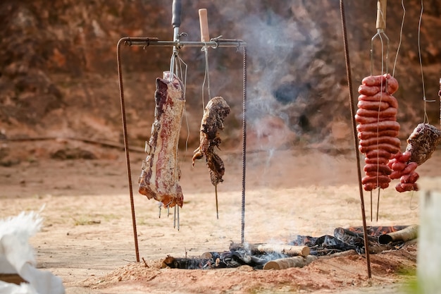 Fleisch braten und schneiden auf dem Tisch und Lagerfeuer mit Feuerholz im Gaucho-Stil