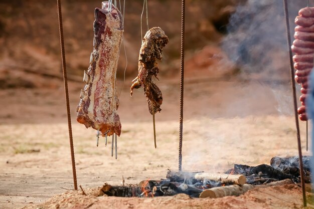 Fleisch braten und schneiden auf dem Tisch und Lagerfeuer mit Feuerholz im Gaucho-Stil