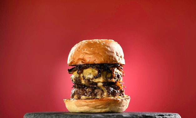 Foto fleisch-cheeseburger mit karamellisierten zwiebeln auf schwarzem teller auf rotem hintergrund