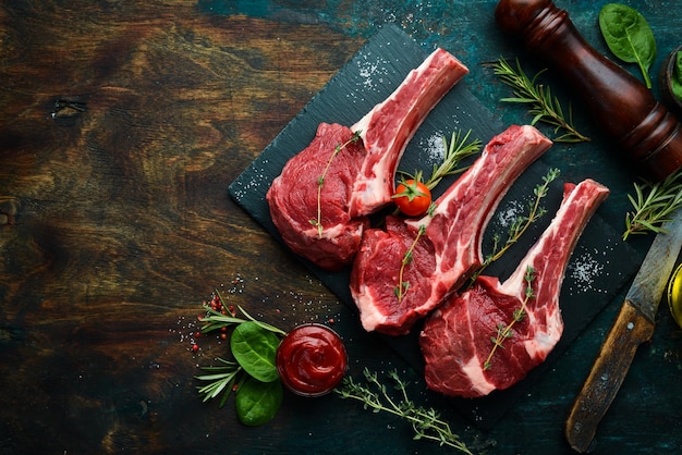 Fleisch Drei rohe Kalbssteaks am Knochen mit Rosmarin und Gewürzen Auf einem schwarzen Steinhintergrund Draufsicht