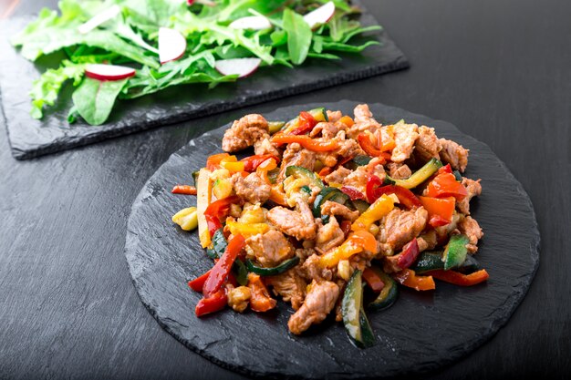 Fleisch mit Gemüse in der Nähe von Salat mit Rucola und Radieschen auf Steinschiefertellern anbraten,