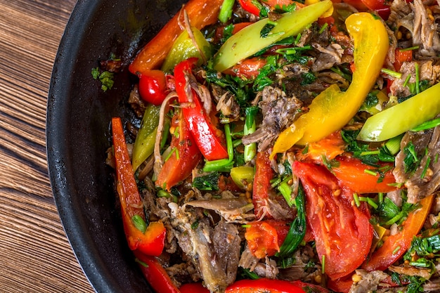 Fleisch mit Gemüse in einer Pfanne auf Holzhintergrund