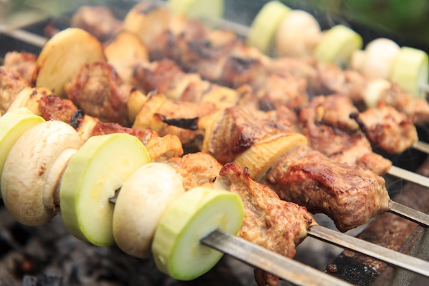 Fleisch und Zwiebeln am Spieß, Zucchini und Pilze am Spieß grillen auf Holzkohle. Kochen eines Tellers Schaschlik beim Grillen. Picknick, Streetfood. Selektiver Fokus