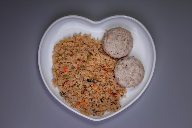 Fleischbällchen aus Hühnerfilet mit garniertem Quinoa mit Gemüse auf hellgrauem Hintergrund