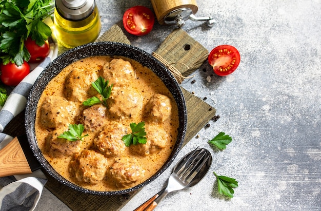 Fleischbällchen in Sauerrahm und Tomatensauce in einer Pfanne auf Steintisch Freiraum für Ihren Text