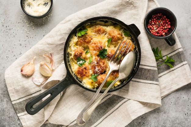 Fleischbällchen mit Käse-Sahne-Sauce in gusseiserner Pfanne auf grauer Vintage-Oberfläche