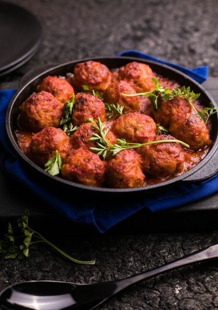 Foto fleischbällchen mit tomatensauce in einer pfanne auf einer schwarzen oberfläche.