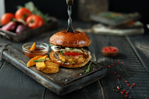 Fleischburger mit Scheiben von Ofenkartoffeln und von Tomatensauce auf hölzernem Brett der Weinlese