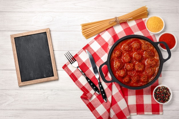 Fleischklöschen in Tomatensauce mit Gewürzen in einer Pfanne auf einem weißen Holzbrett