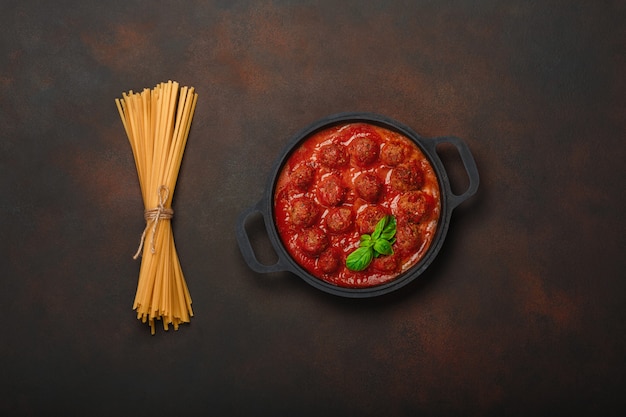 Fleischklöschen in Tomatensauce mit Gewürzen, Teigwaren und Basilikum in einer Pfanne auf rostigem braunem Hintergrund