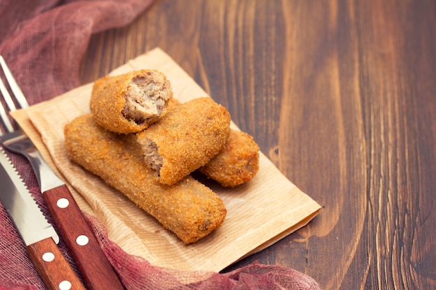 Fleischkroketten auf Papier auf hölzernem Hintergrund