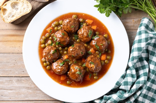 Fleischkugeln, grüne Erbsen und Karotten mit Tomatensauce auf einem Holztisch