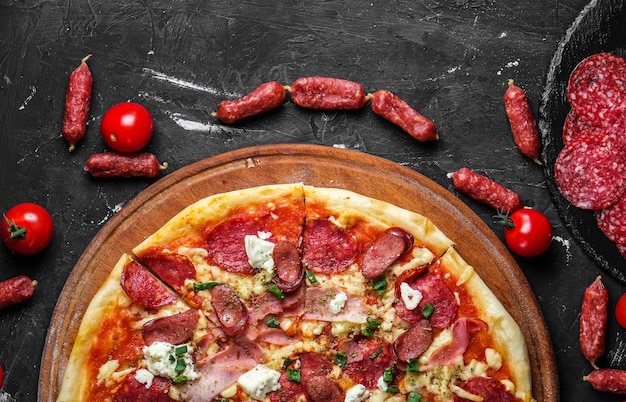 Fleischpizza mit Salami, Schinken, Huhn, Würstchen und Feta-Käse, auf einer Tafel und auf einer dunklen Oberfläche