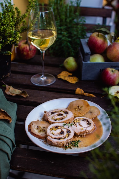 Fleischroulade füllte mit Pistazien und Pflaumen, Weißweinglas auf rustikalem Holztisch