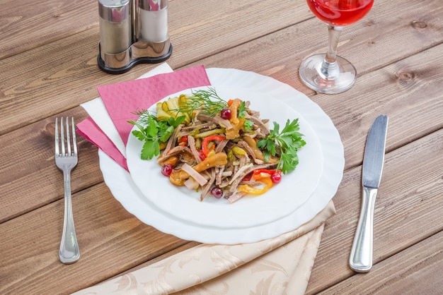 Fleischsalat mit gedünstetem Gemüse und Champignons dekoriert mit Kräutern auf einem weißen Teller